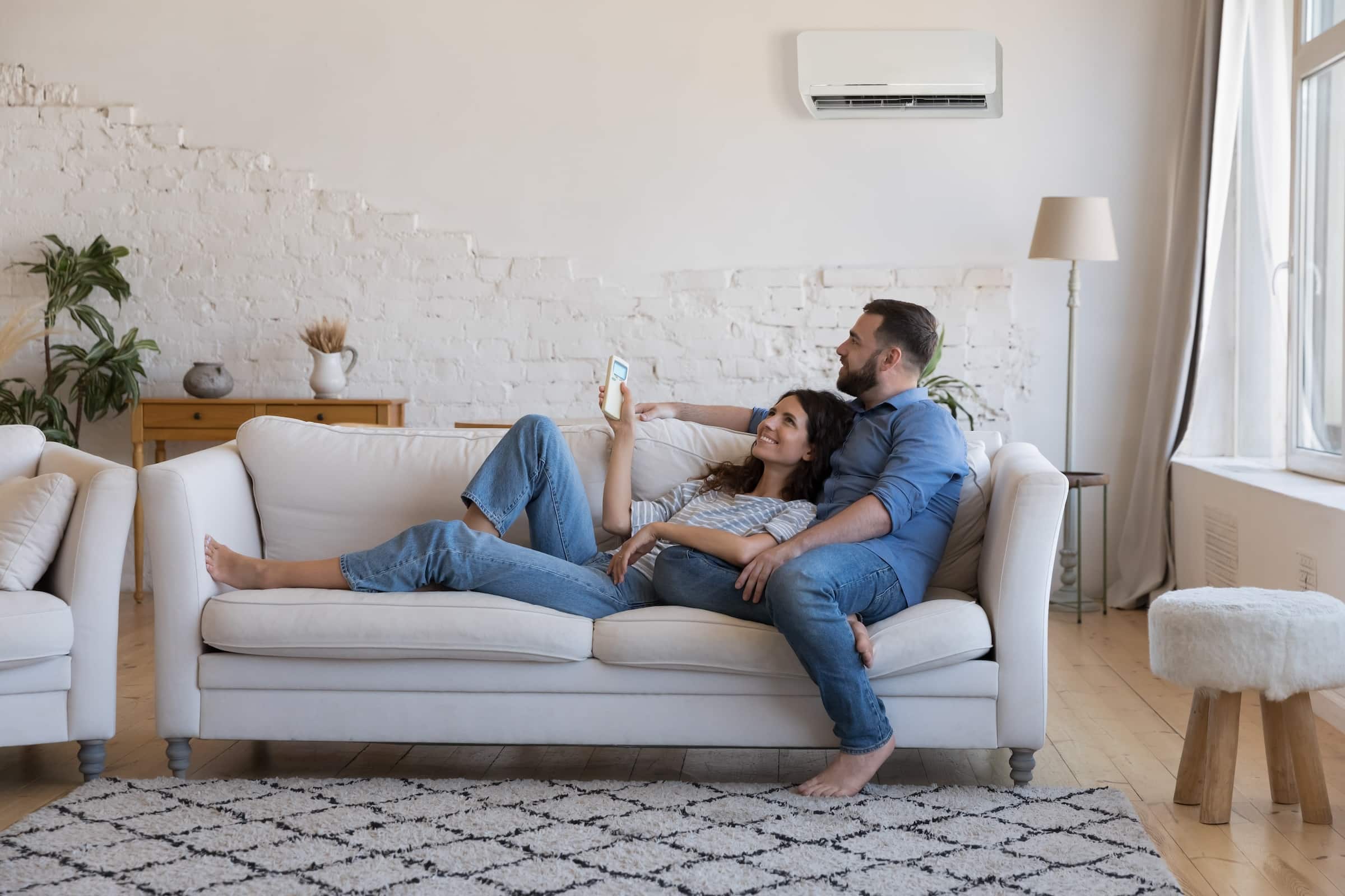 Couple laying on couch with ductless mini-split heat pump on the wall in the background