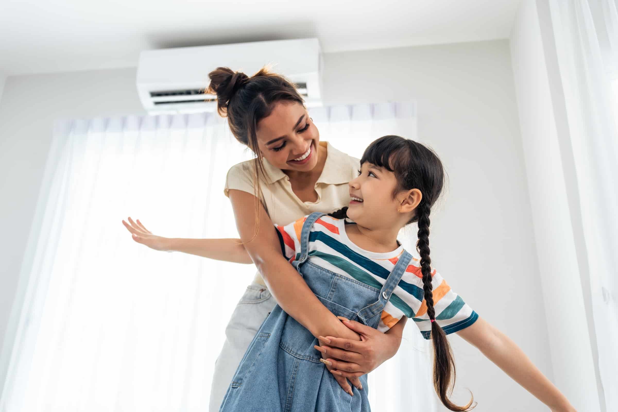 Happy Mom hugging daughter while mini-split air conditioner runs in the background